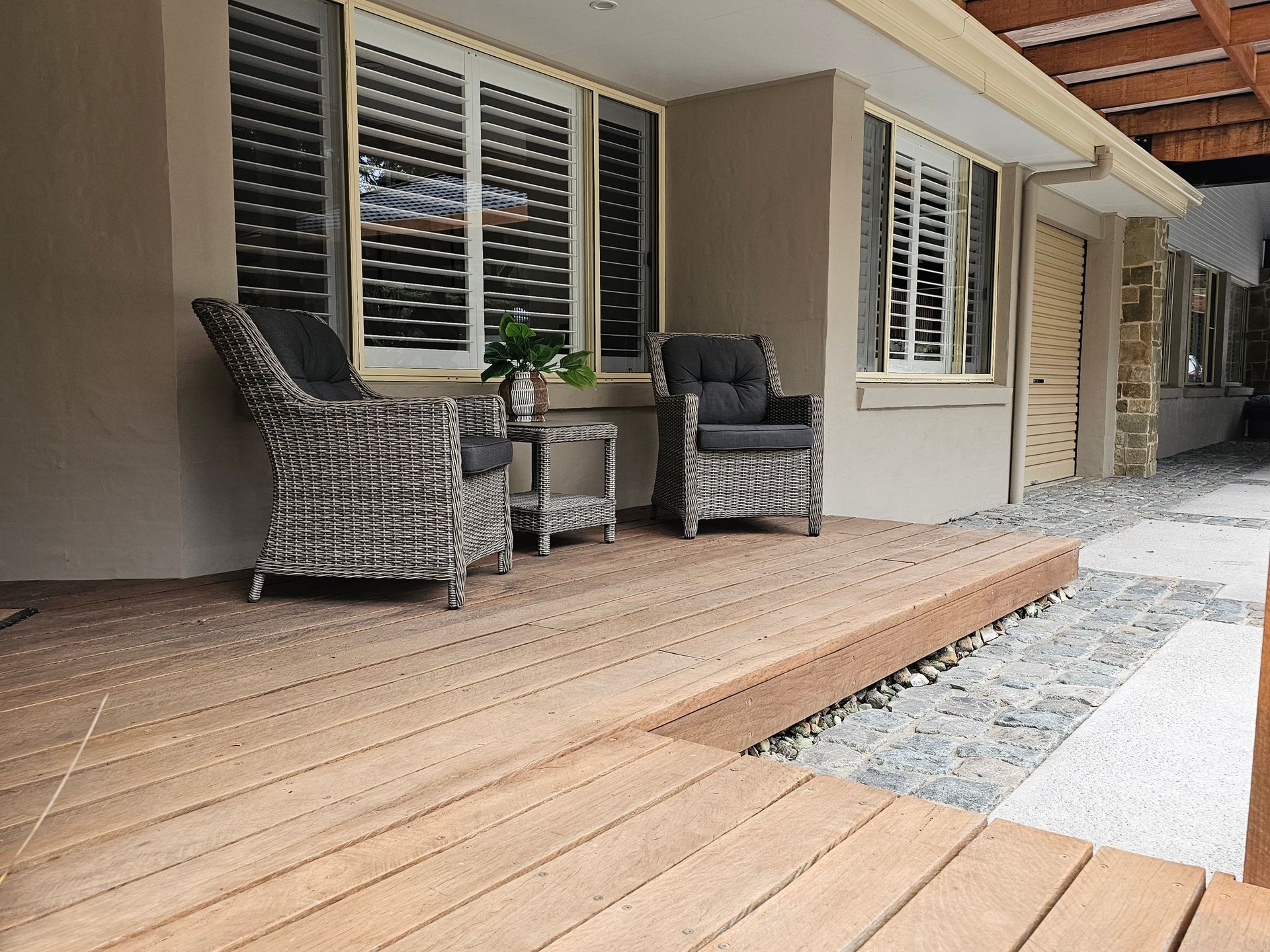 Wooden deck with wicker chairs and a small table near a building with shutters.