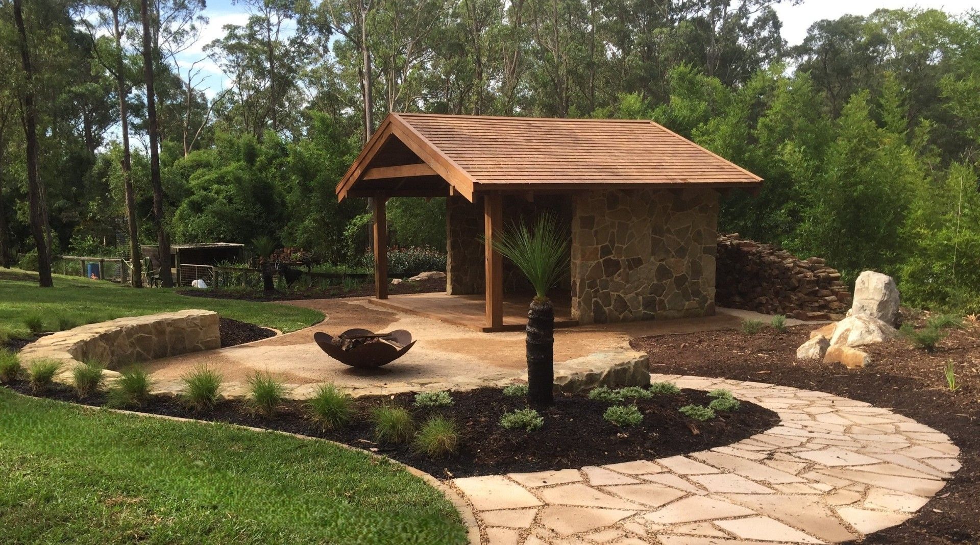 Small building under construction with a concrete block base, wooden roof, and surrounding greenery.