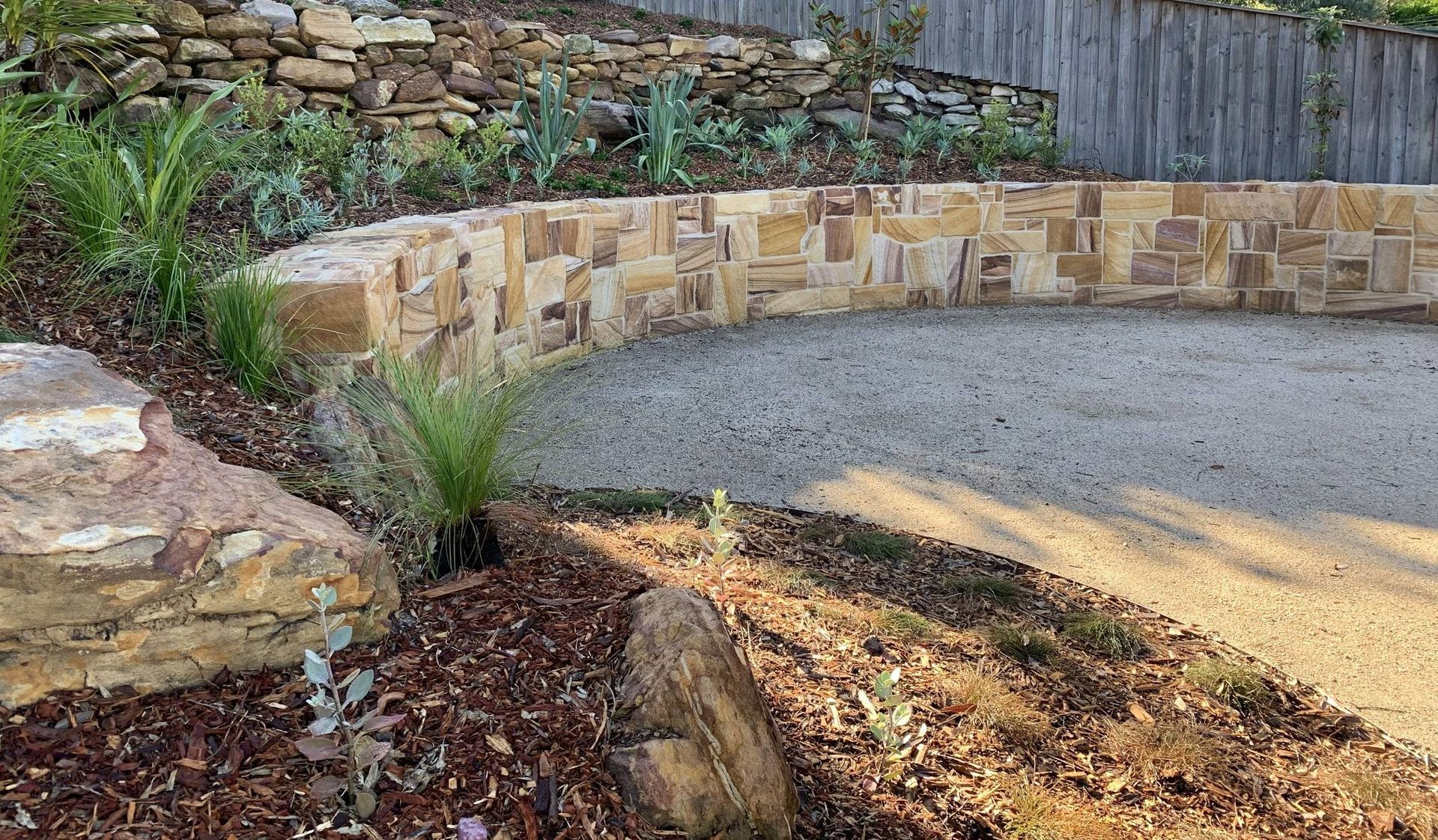 Curved stone retaining wall with gravel drive and planted border.