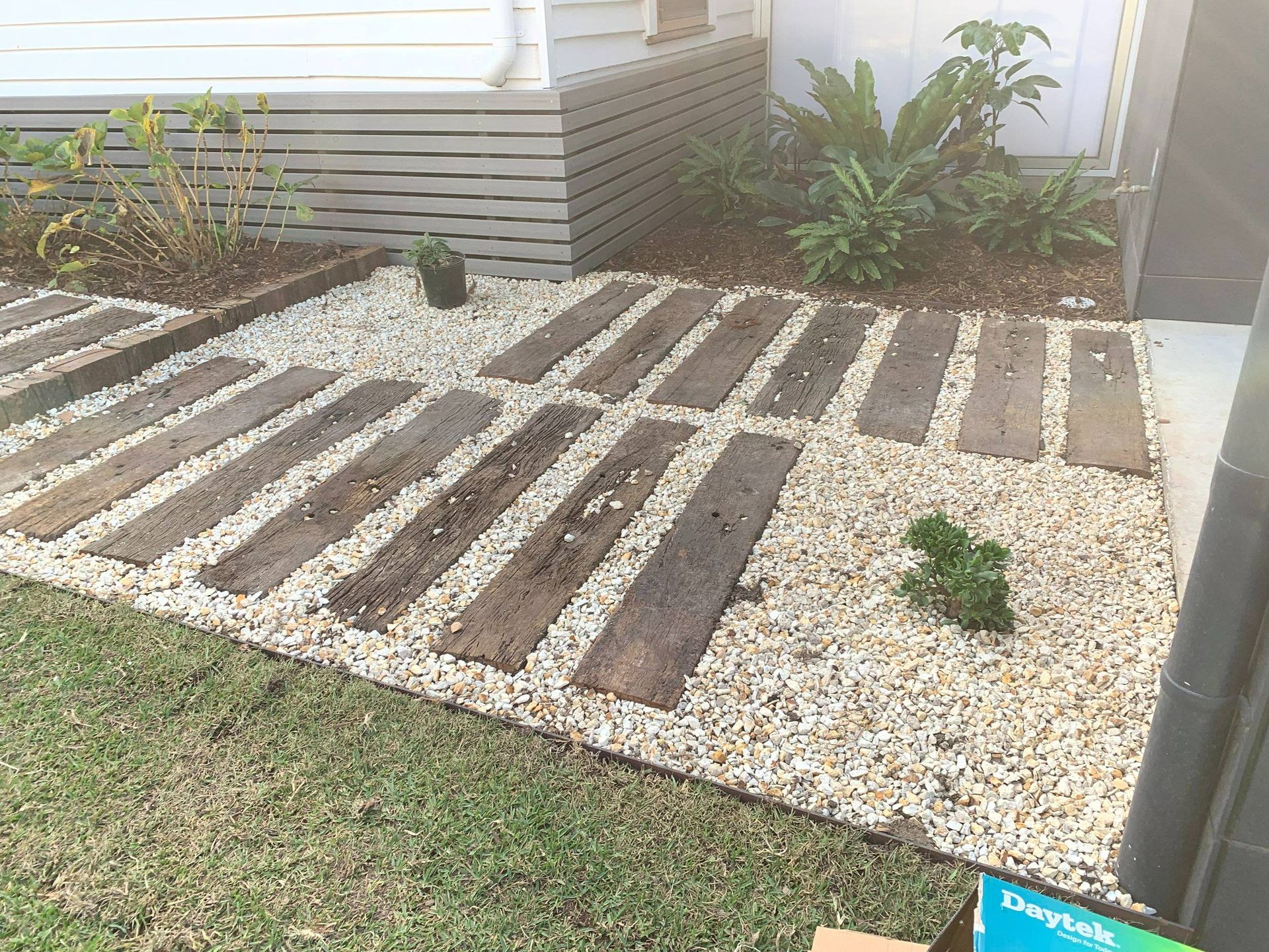 Pathway of wooden planks set in gravel. Green grass surrounds.