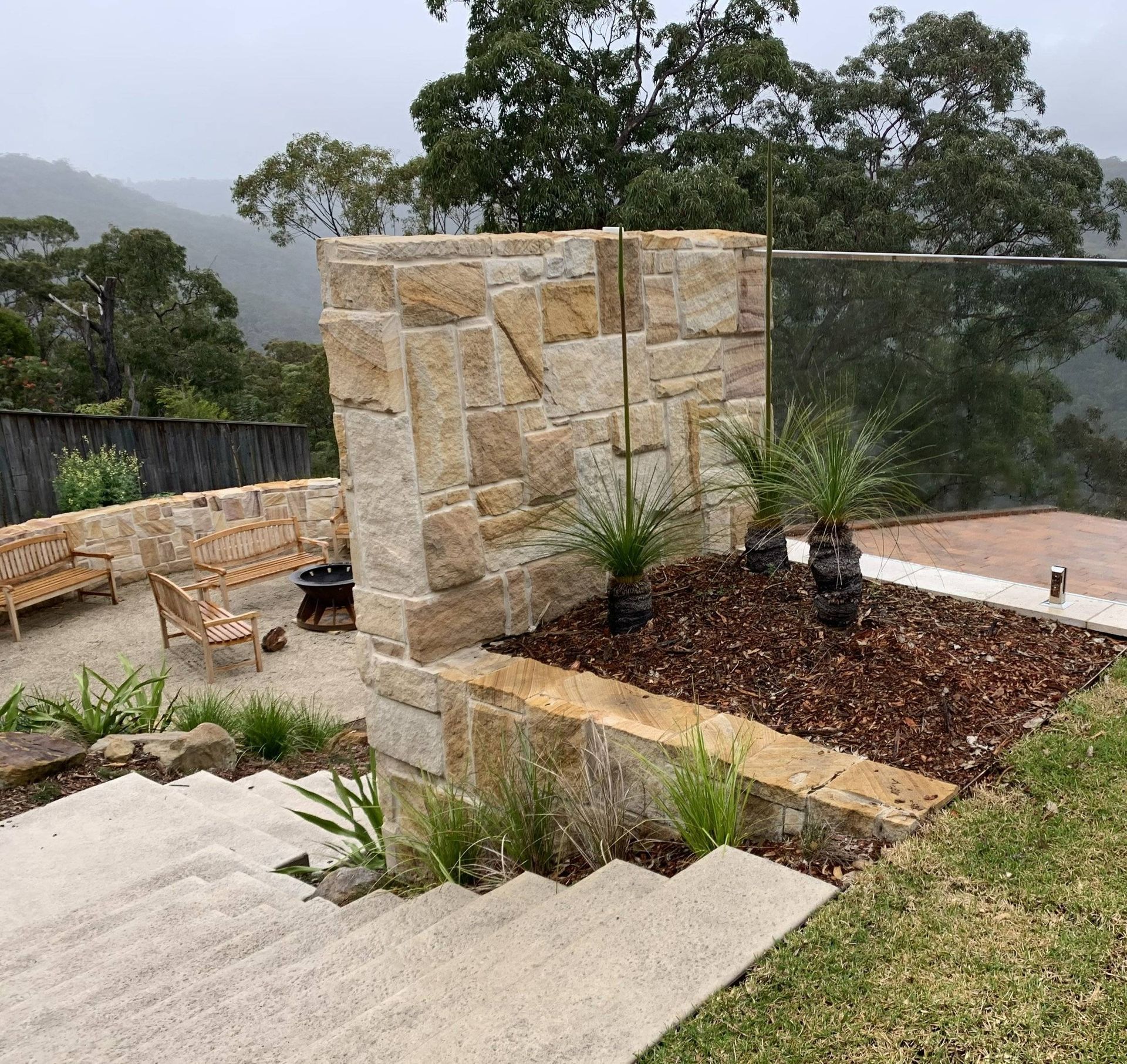 Stone wall with plants, steps, seating, and scenic view.