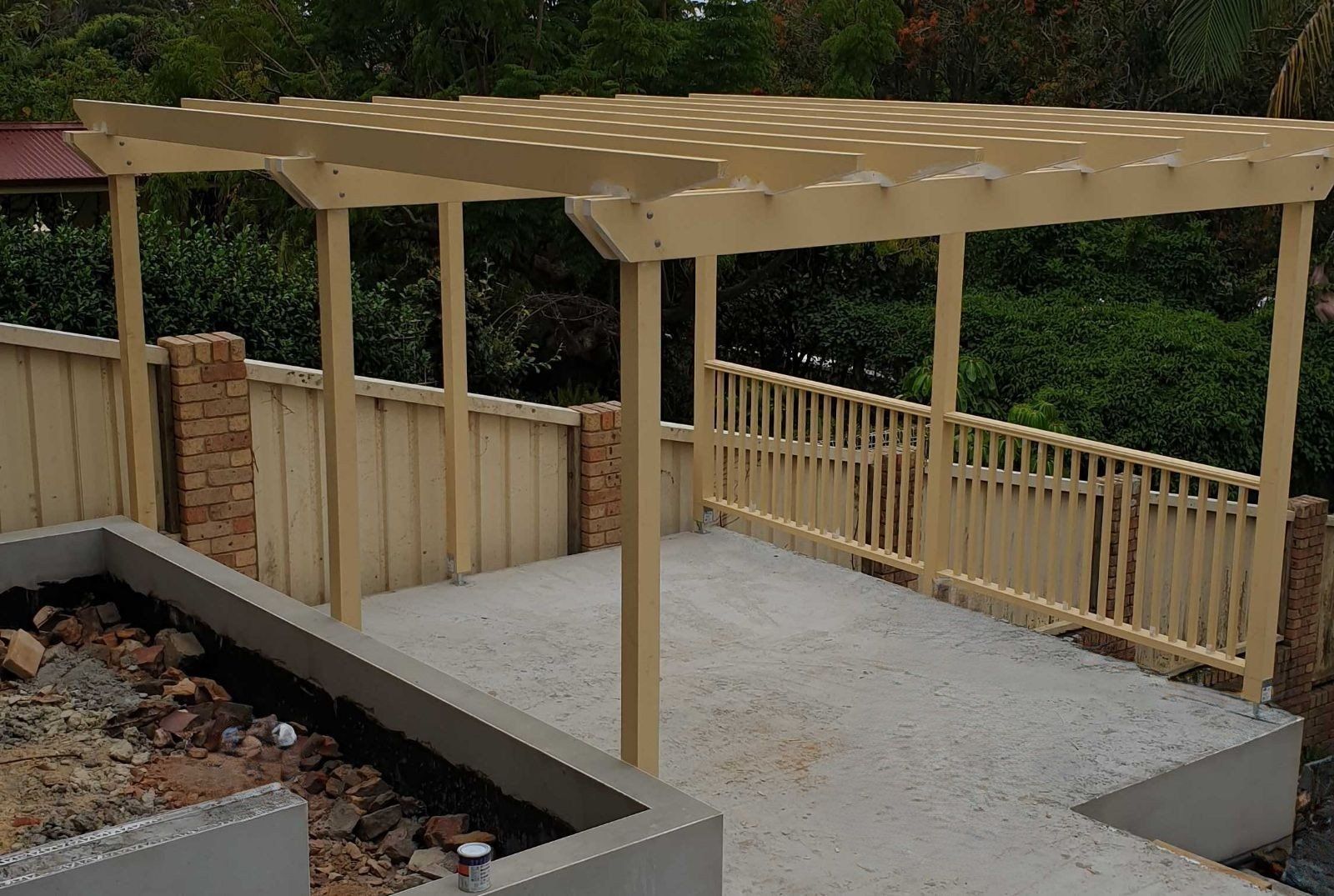 Wooden pergola over a concrete patio next to a fence and landscaping.