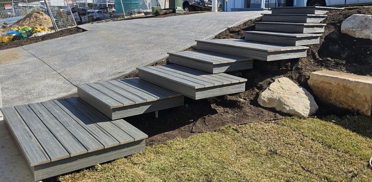 Gray wooden steps leading up a grassy hill, with gravel pathway and large rocks.