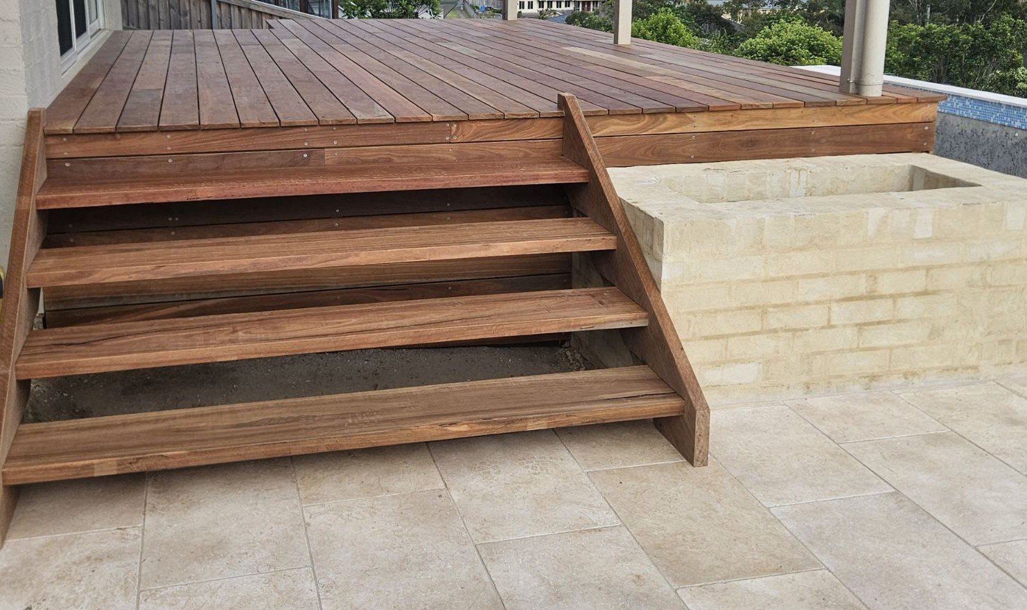 Wooden stairs leading up to a wooden deck, next to a light-colored brick structure.