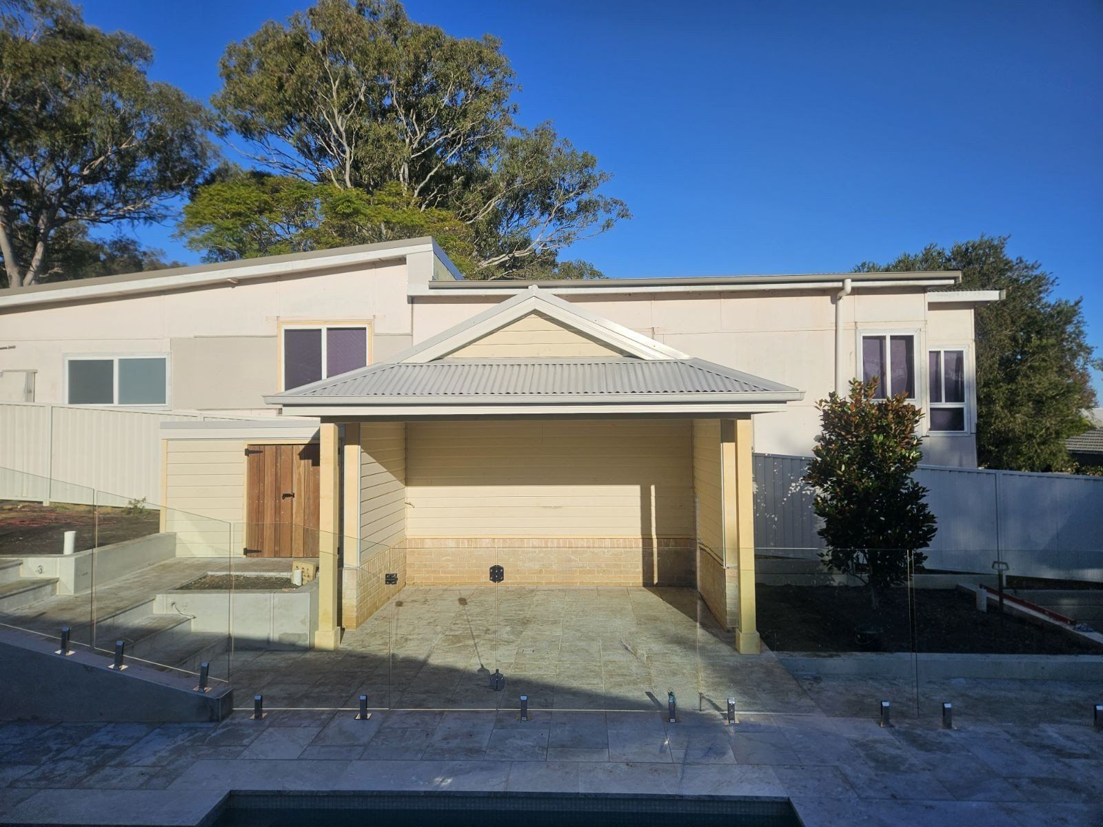 Beige and white modern house with a carport; blue sky, trees in background.