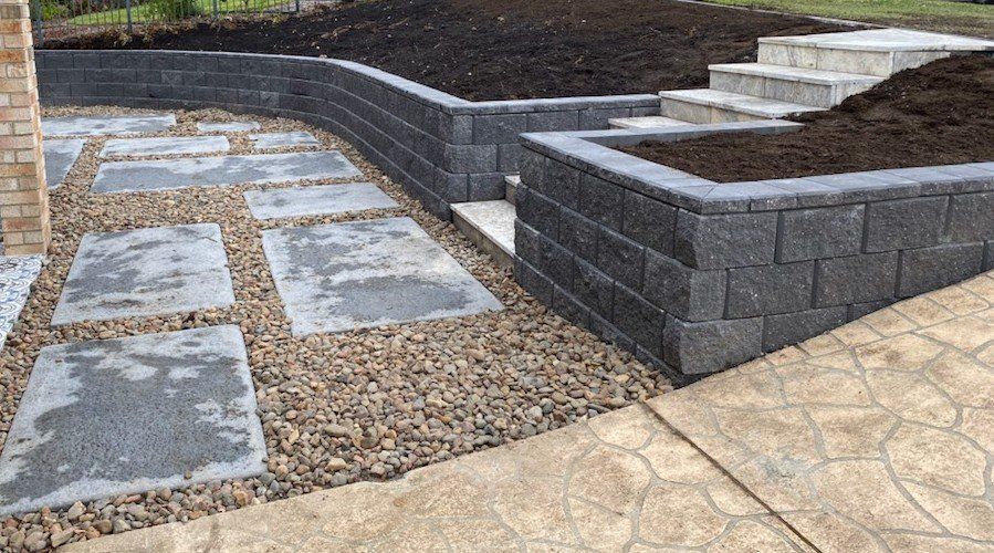 Outdoor landscaping with stone pavers, retaining walls, and steps.