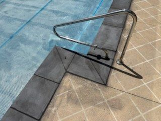 Pool coping with a handrail and blue pool cover.