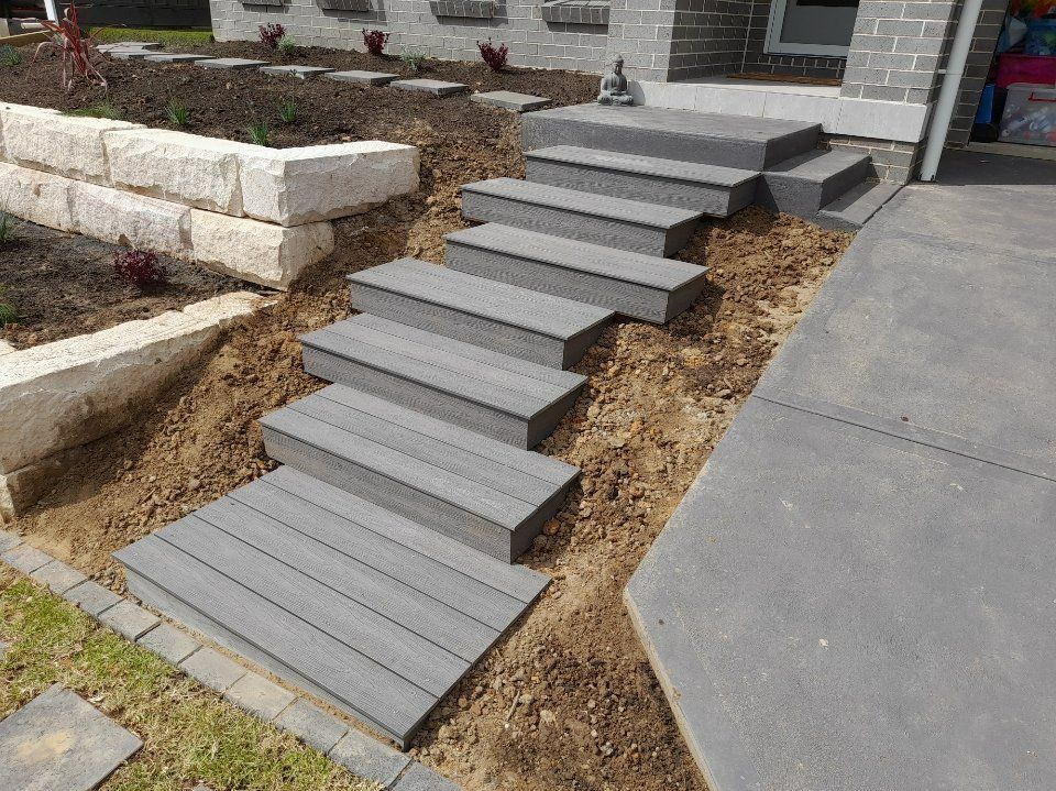 Stone steps leading up to a house entrance, next to a retaining wall and driveway.