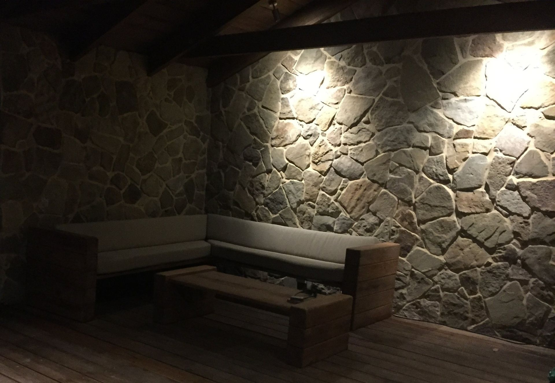 Stone wall with sofa and coffee table lit by overhead lights.