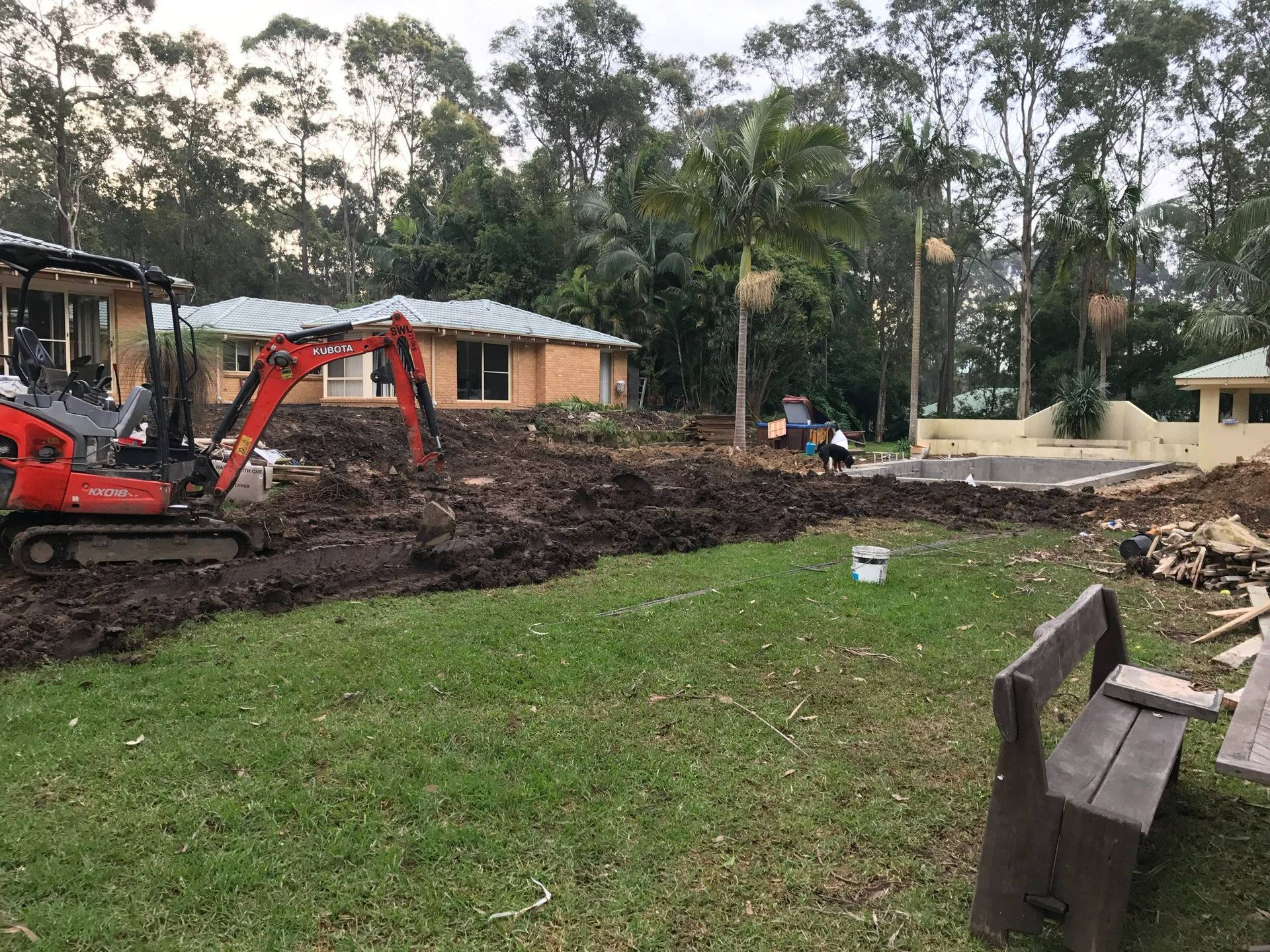 Construction site: Mini excavator digs up dirt in a backyard with houses and trees.