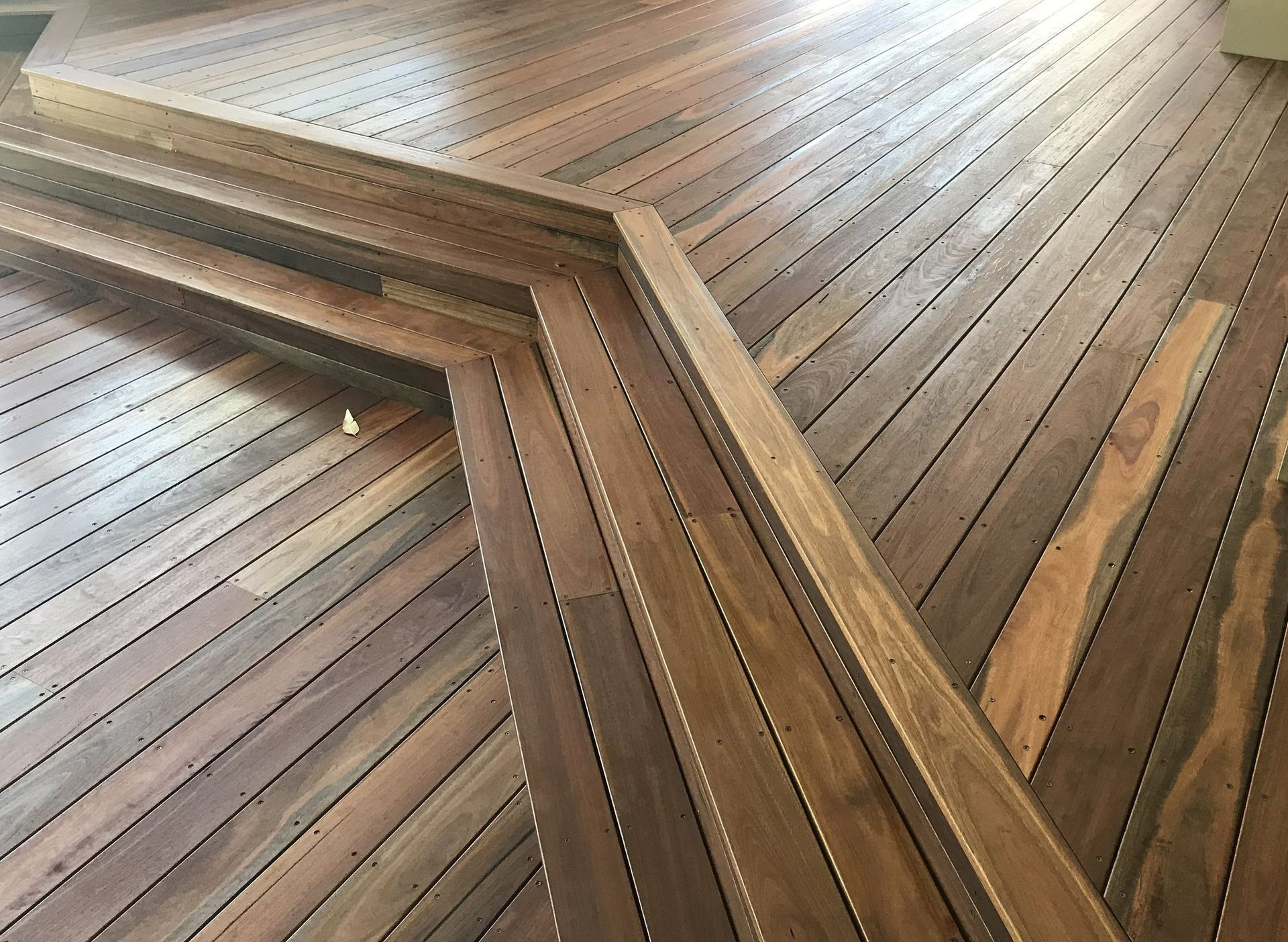Wooden deck with built-in steps and handrail; angled planks create a patterned surface.