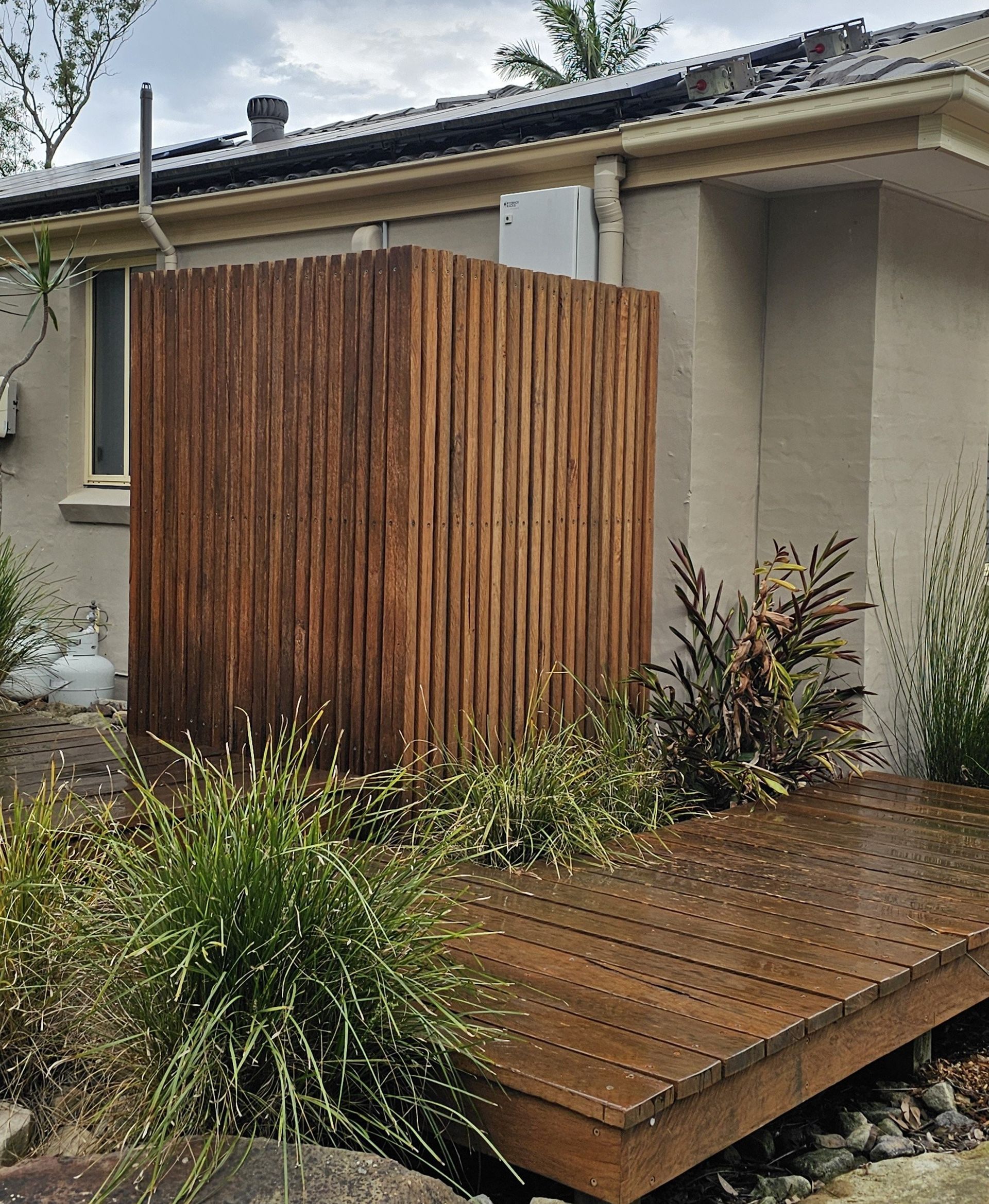 Wooden outdoor shower with a wooden deck and surrounding greenery.