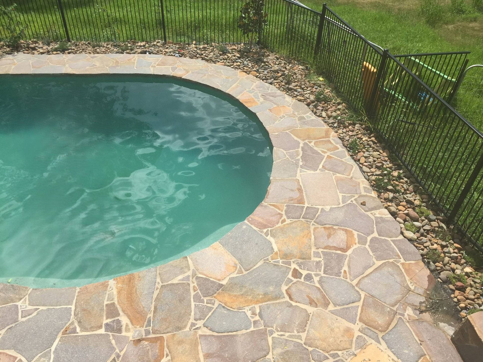 Swimming pool with stone paving and black fence.