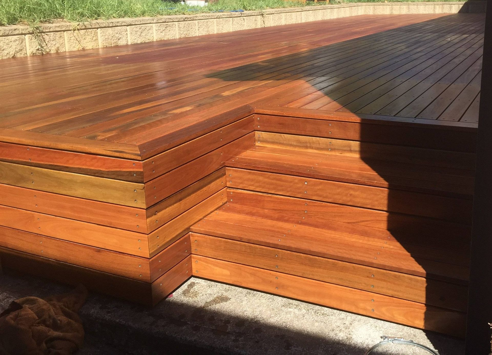 Wooden deck with multiple levels, featuring steps. The wood is stained a warm, reddish-brown color, and it appears freshly sealed.