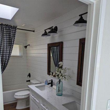 Bright bathroom with white shiplap walls, double vanity, mirrors, and a toilet near a window.