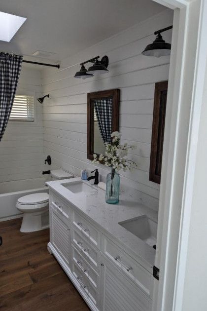 Bright bathroom vanity with white cabinets, wood floor, mirror, sink, and toilet near a shower curtain.