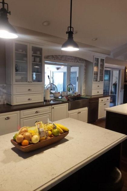 Bright kitchen with island, fruit bowl, pendant lights, and cabinets around a central window.