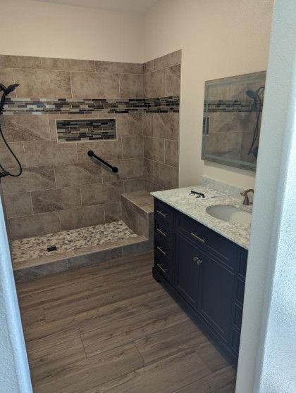 Modern bathroom with tiled walk-in shower, dark vanity, and wood-look floor.