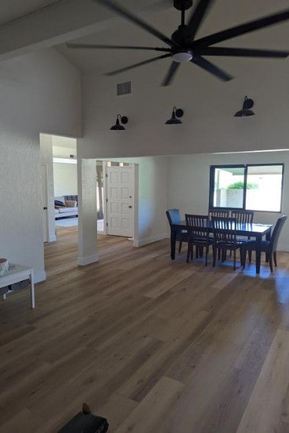 Spacious modern dining area with wood floors, ceiling fan, blue chairs, and large window.