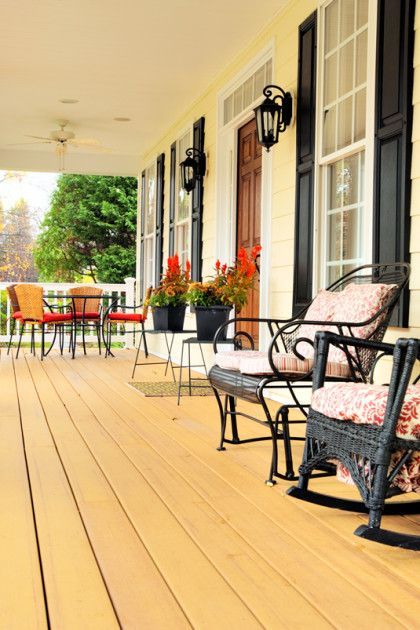 Covered porch with black rocking chairs, potted flowers, and colorful patio seating on a wooden floor.