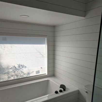 White bathroom with shiplap walls, a bathtub, and a window with a blind.