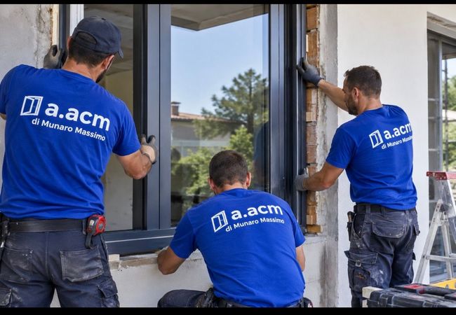 Tre operai con magliette blu installano un telaio per finestra sulla facciata di un edificio
