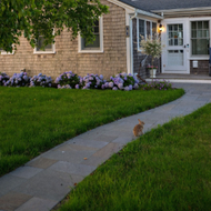 Two-story house with teal accents and front porch, set on a grassy lawn under an overcast sky