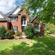 Person mowing grass in a front yard beside a brick path and house porch.