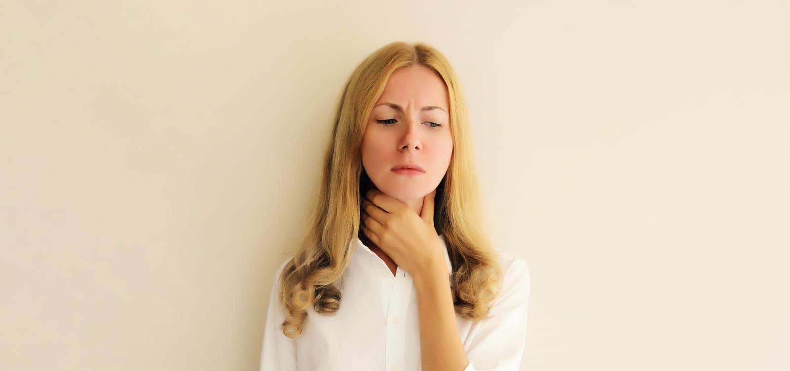 Woman with blonde hair touching her neck, indicating throat pain