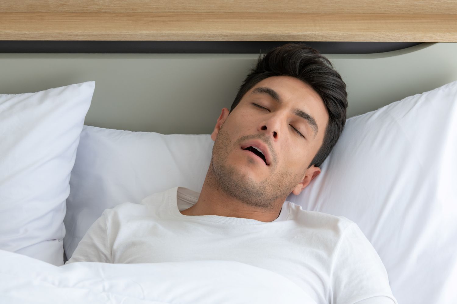 Person sleeping in a bed with white sheets and pillows, mouth slightly open