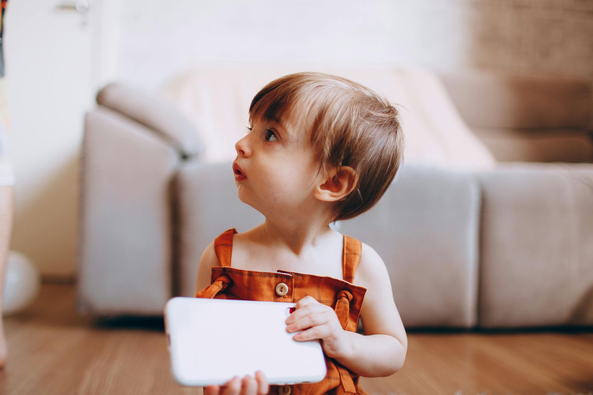 Young child with hearing loss holding a white card and looking upward in a living room