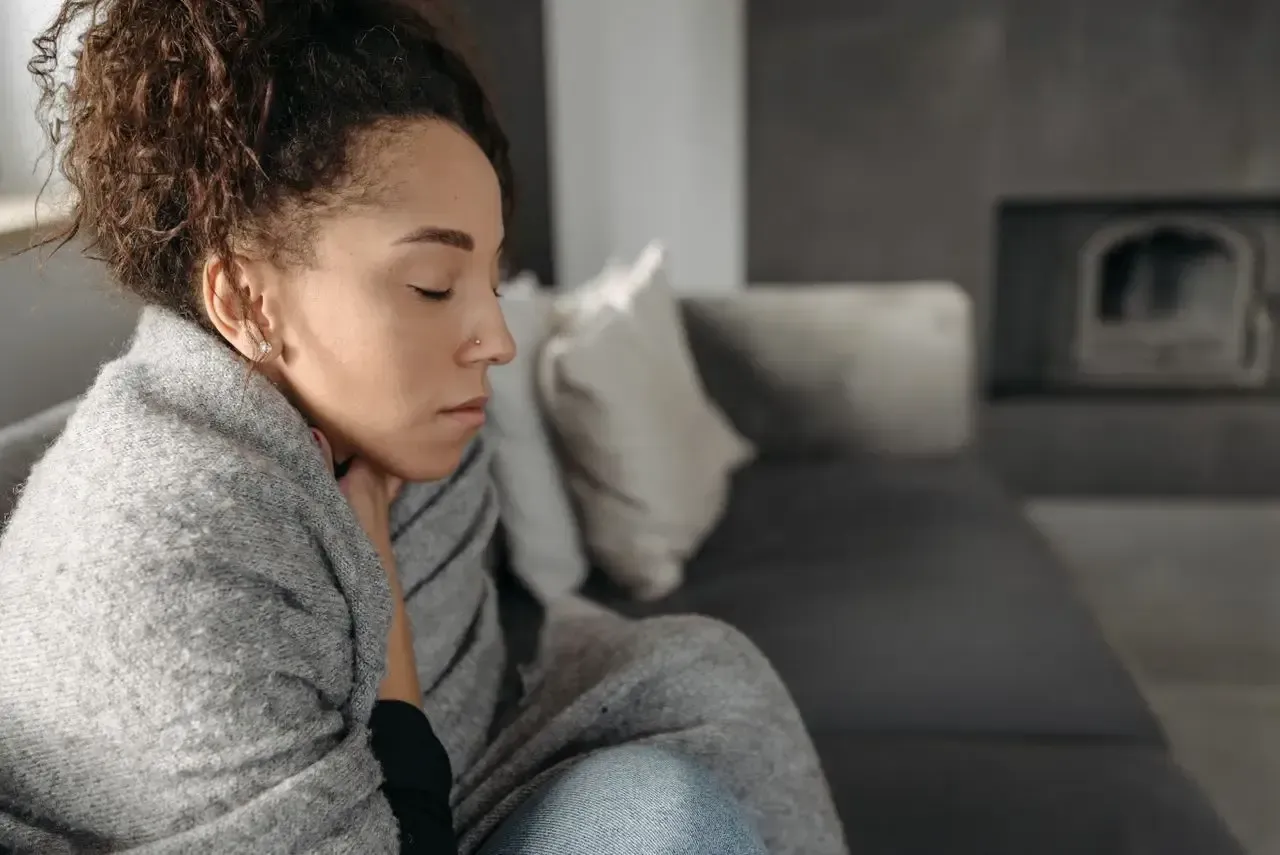 Woman sitting in a living room experiencing throat pain associated with tonsillitis