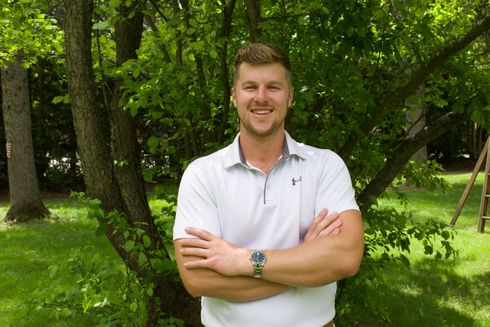 Man standing with arms crossed in a green park, wearing a white shirt and smiling