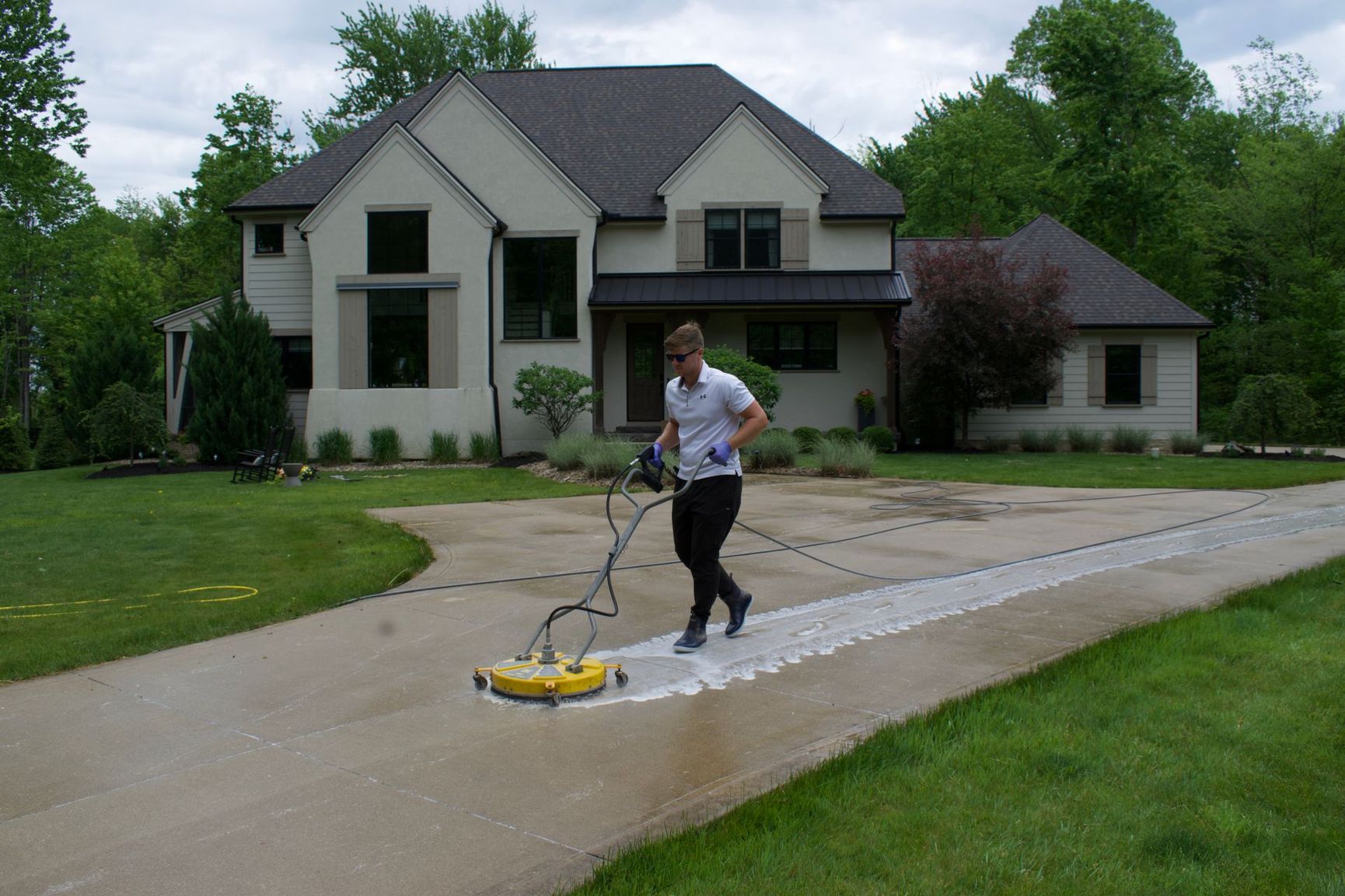 Person power-washing a driveway in front of a house and garage