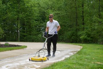 Person using a yellow floor scrubber on a paved path in a wooded park