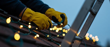 Worker in yellow gloves installing string lights on a rooftop at dusk