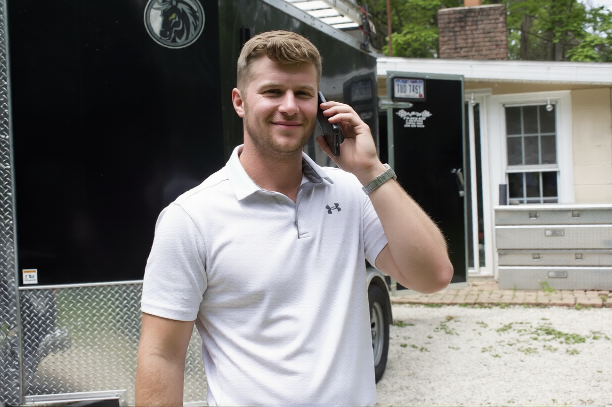 Man in white polo shirt standing by a truck, holding a phone to his ear outside a house