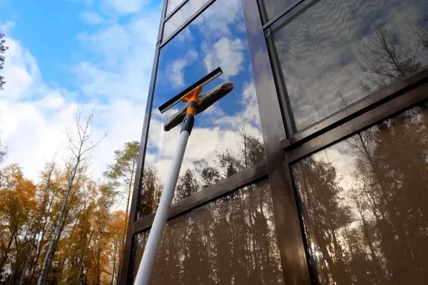 Window-cleaning pole reaching up to a reflective glass building under a blue sky