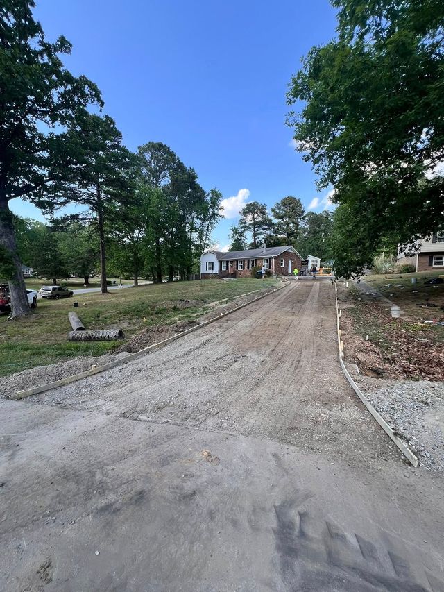 Gravel driveway leading to a house under construction, surrounded by trees on a sunny day