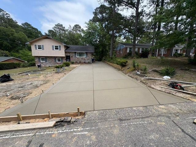 Fresh concrete driveway leading to a beige house, with construction materials and trees nearby