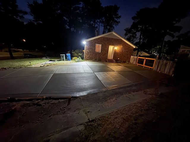 Nighttime view of a brick building with bright exterior lights and a wet driveway in front
