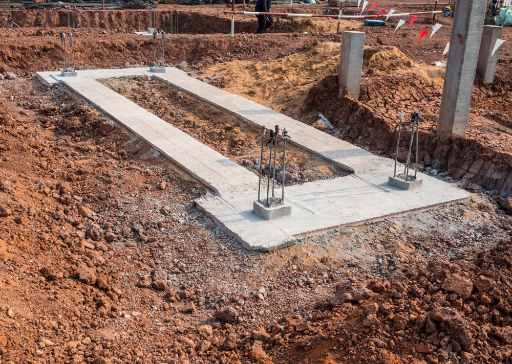 Foundation slab and rebar footings at a construction site with dirt and concrete forms