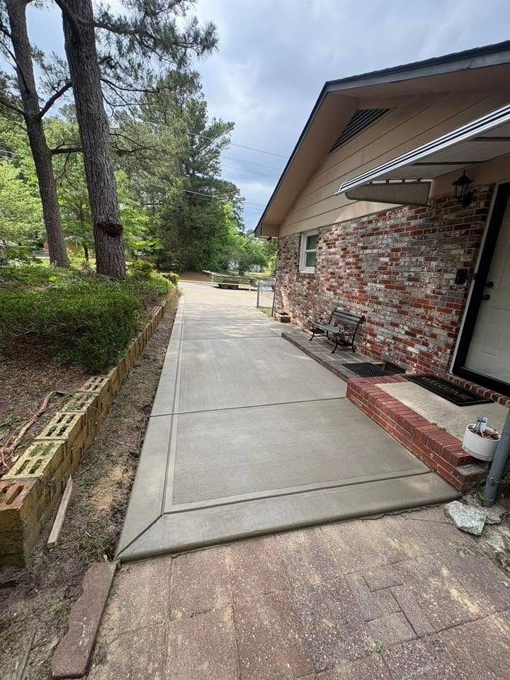 Concrete walkway beside brick house and trees in a landscaped yard