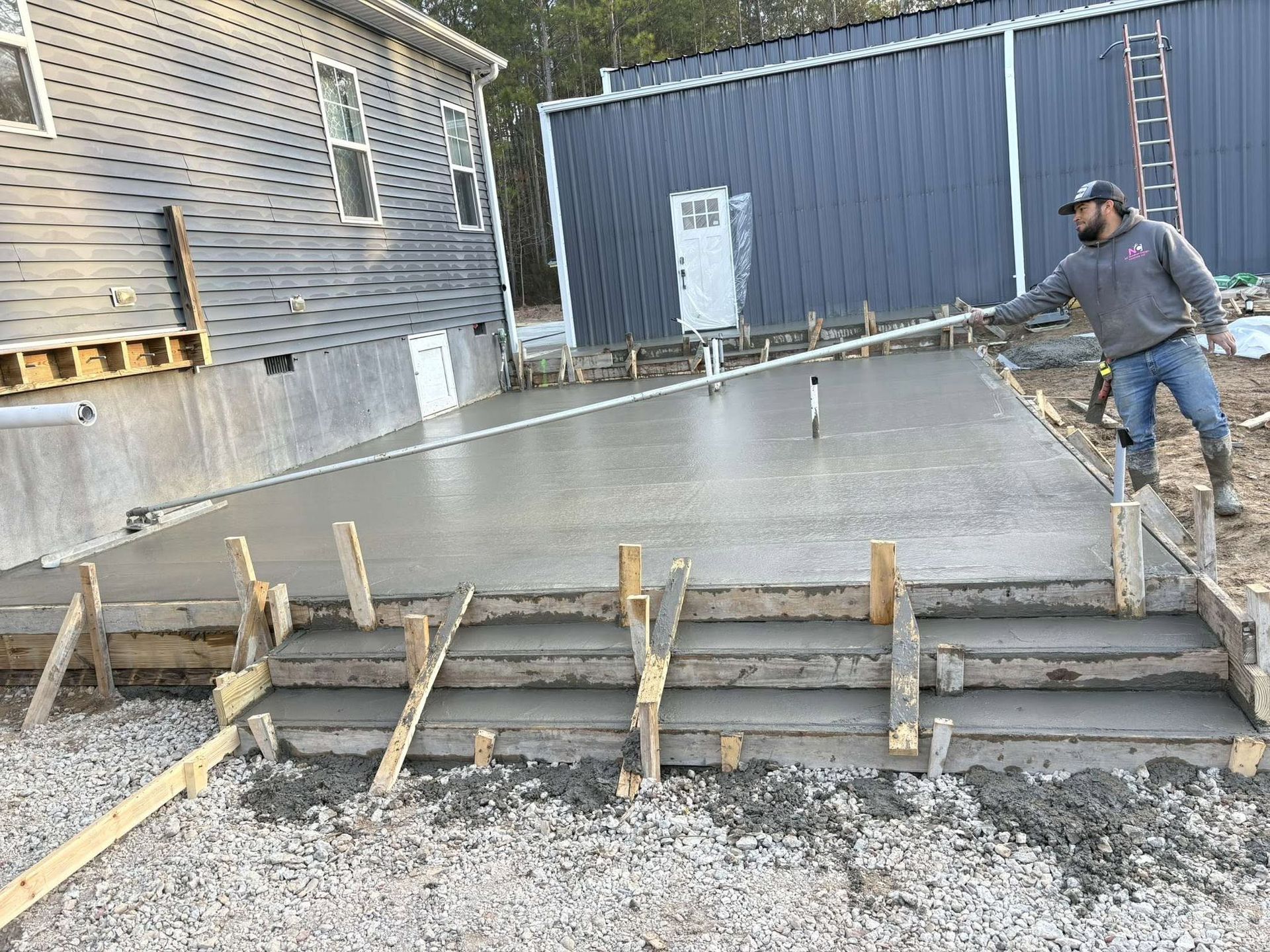 Worker smoothing fresh concrete beside wooden forms at a construction site
