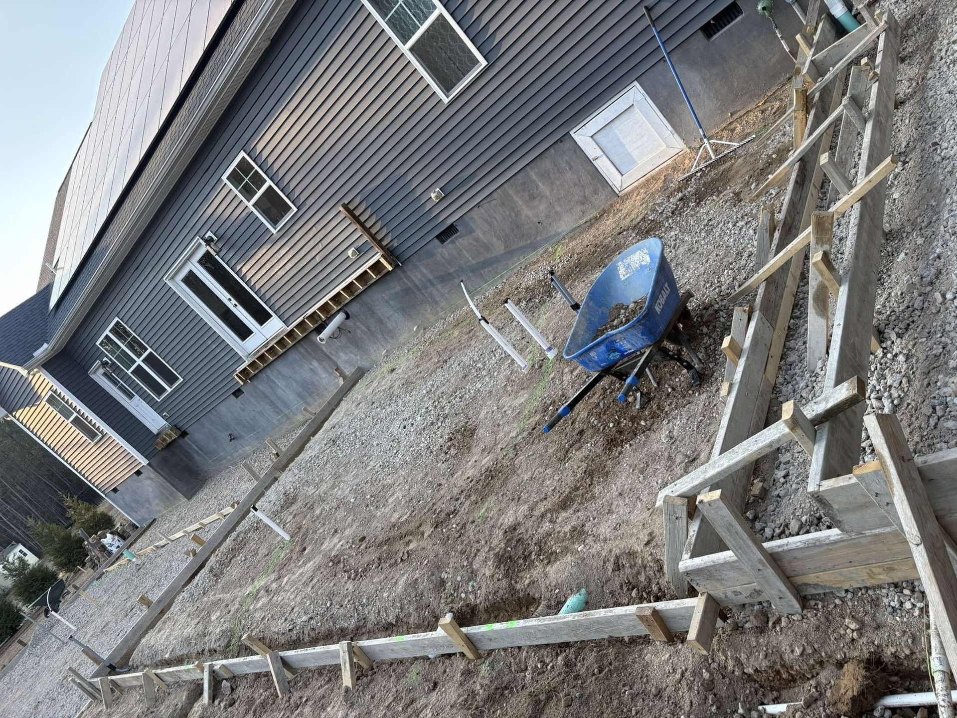 Backyard with raised wooden fence, gray house, and blue wheelbarrow on snowy ground