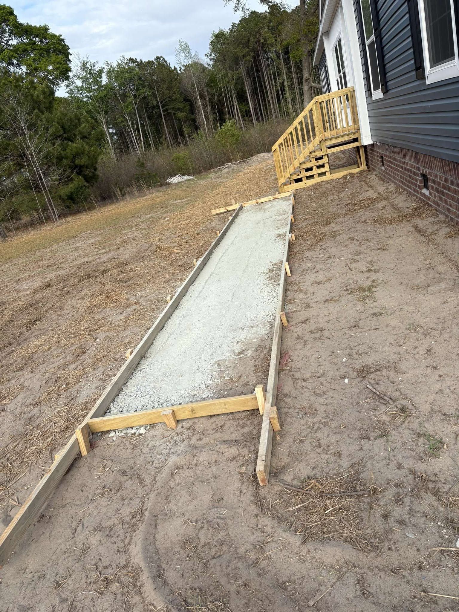 Concrete walkway form beside house with wooden braces and gravel yard
