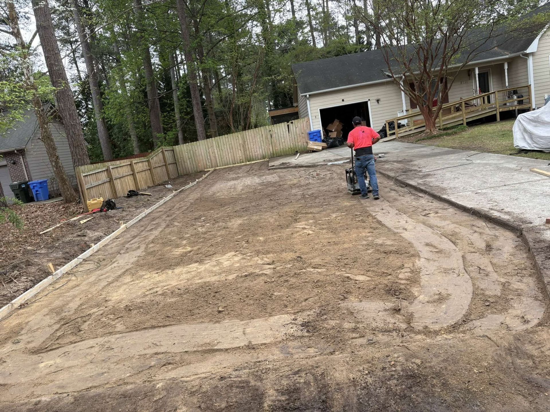 Person in red shirt on a gravel driveway near a garage and fenced yard
