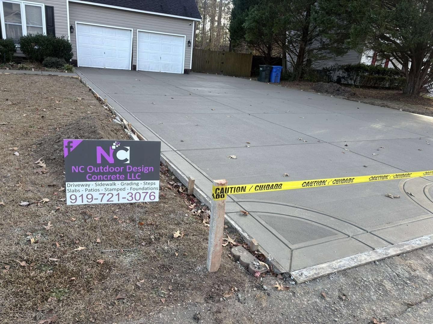 Driveway with a collapsed concrete edge near yellow caution tape and an NC Outdoors sign by a garage