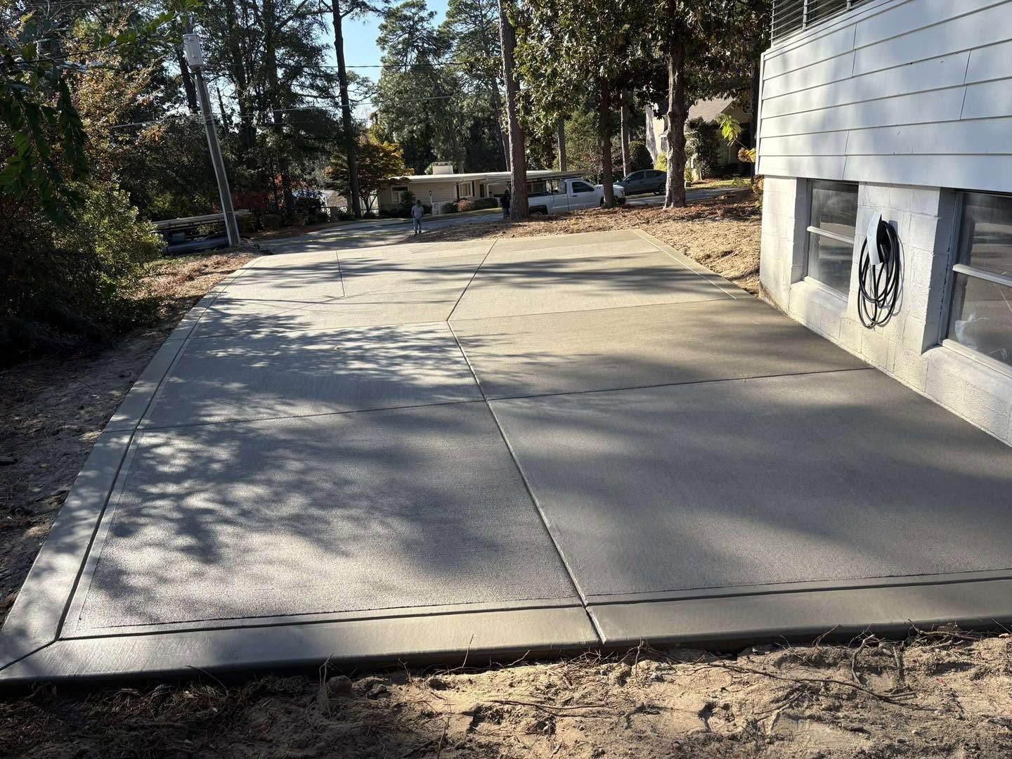 Concrete driveway beside a white building, leading through a tree-lined outdoor area.