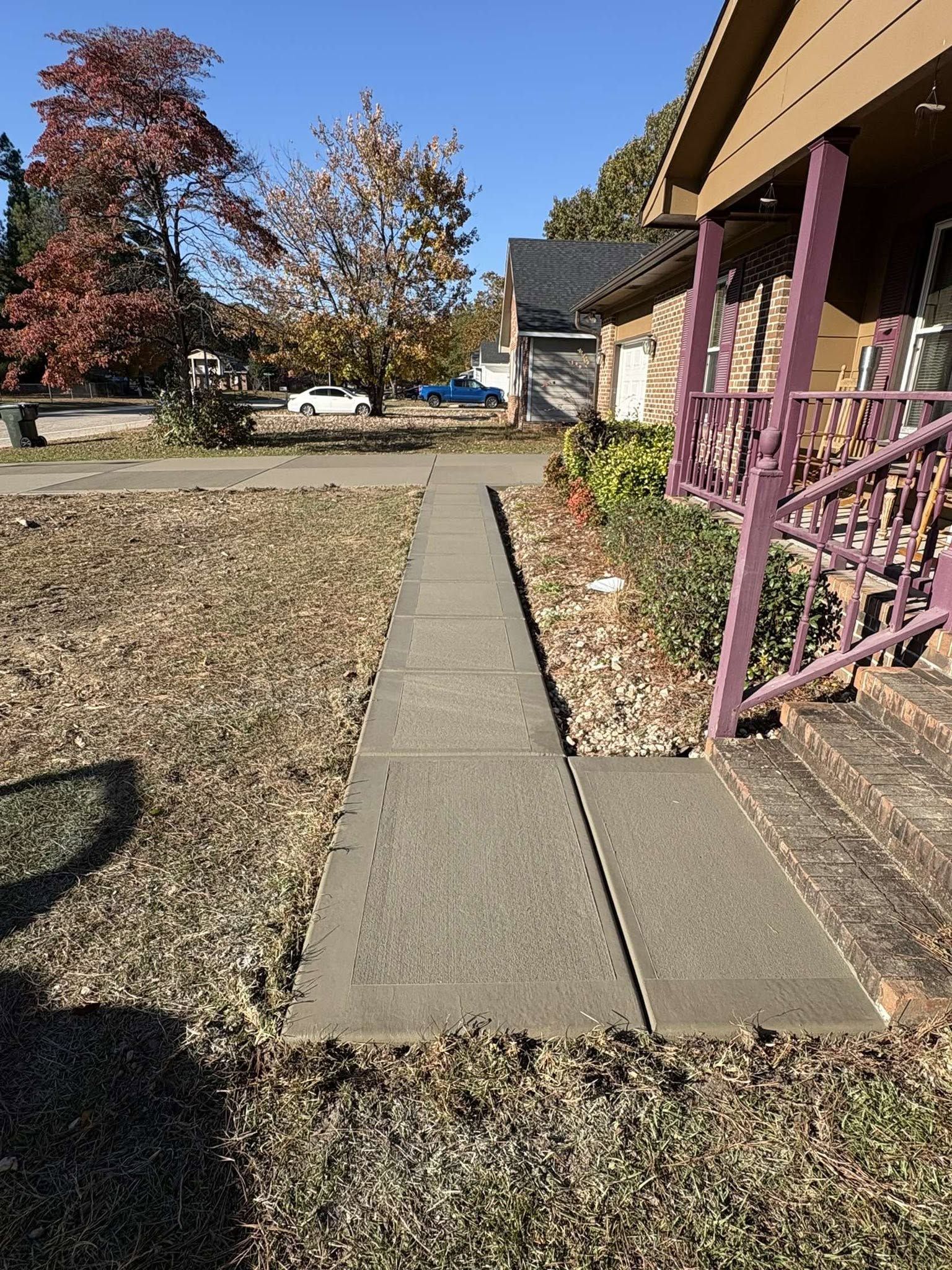 Concrete walkway leading to a house porch beside a gravel yard and autumn trees